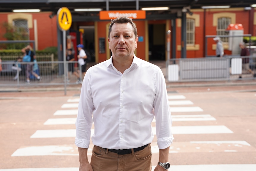 Man standing in a shirt and pants at a railway station.