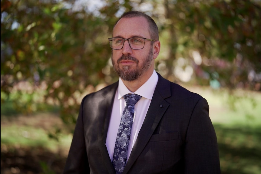 Jarrod Carter standing in a leafy outdoor area in the shade and wearing a suit.