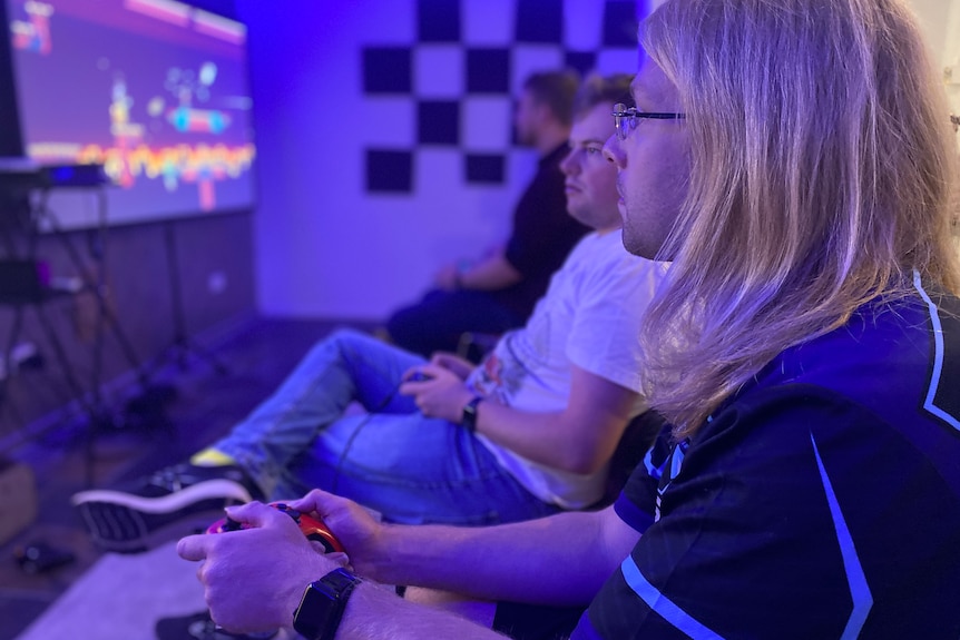 Three men sit playing Mario Kart on a television screen.