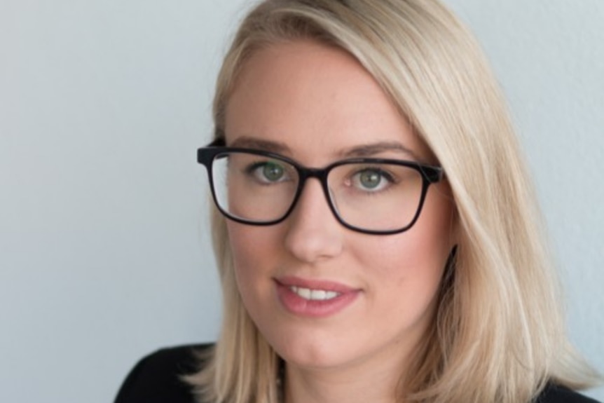 Head and shoulders photo of blonde woman in glasses wearing dark jacket.