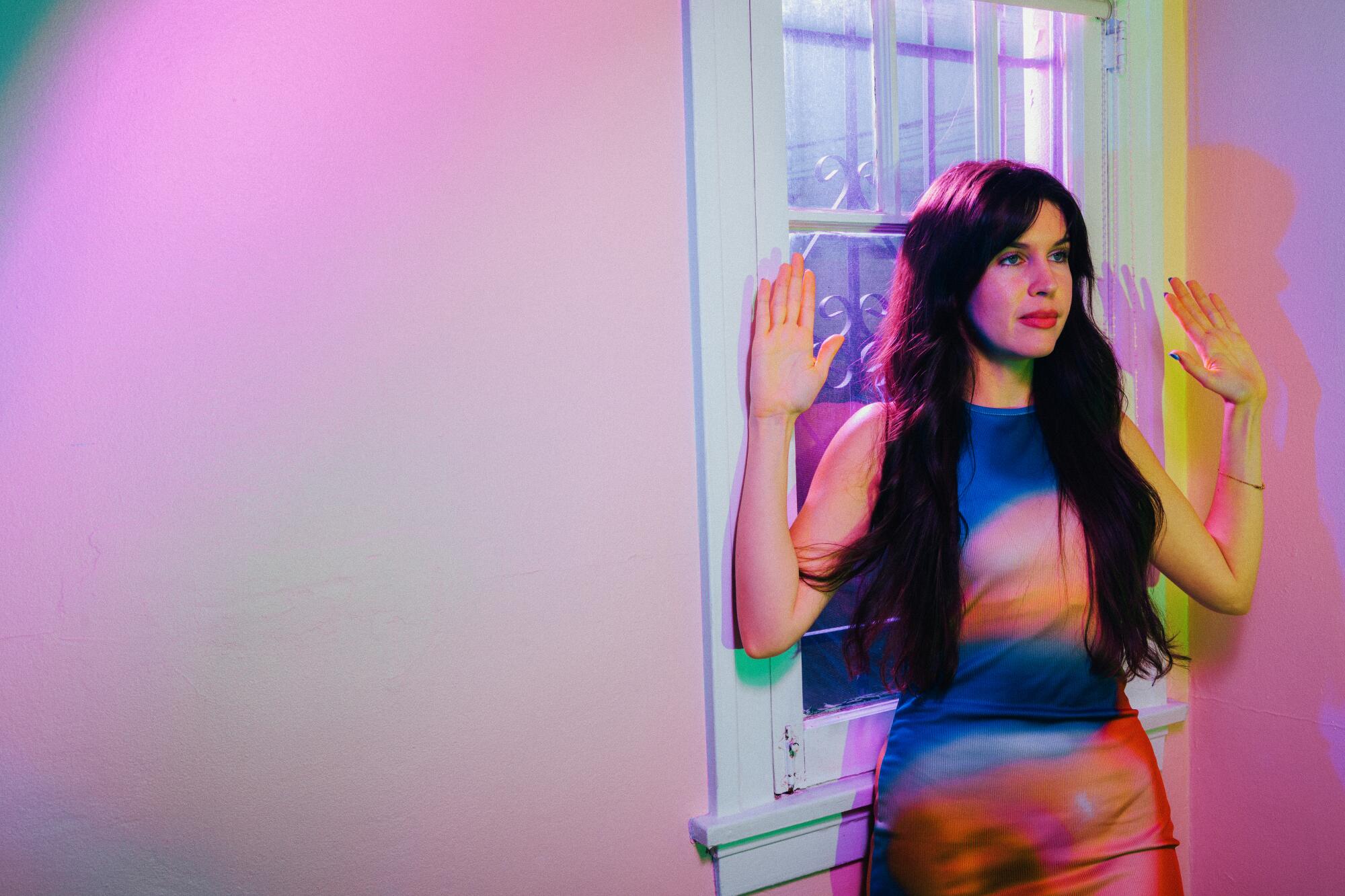 Han Santana-Sayles stands by a window in her Pasadena home with her hands up. 