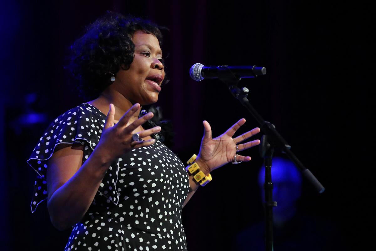 A woman in a white-dotted black dress sings at a microphone. 