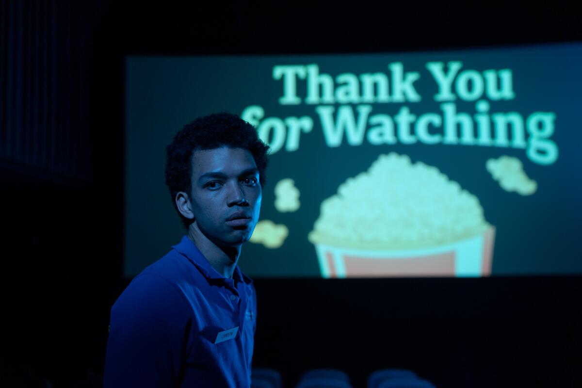 A young man walks down a movie theater aisle.