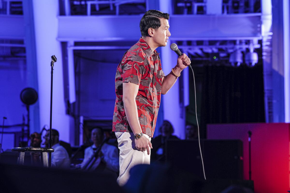 Man on stage in red shirt holding a microphone