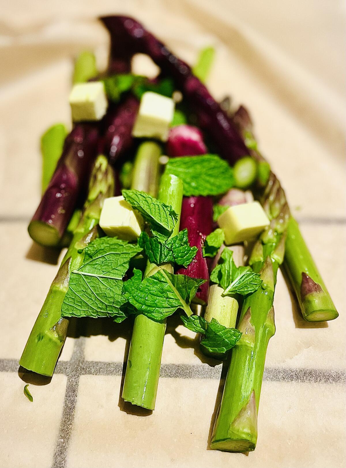 An assortment of California-grown asparagus with mint and butter about to be bundled in parchment and roasted in the oven.