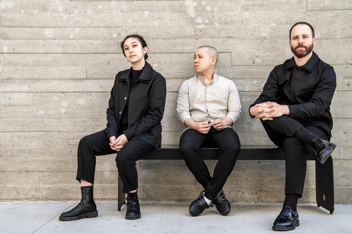 Three people sit outside on a bench in front of a stone wall