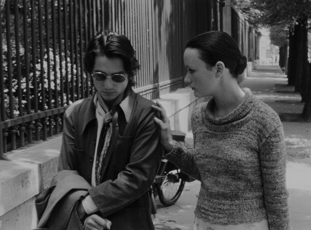 Two French people walk down the street, speaking.