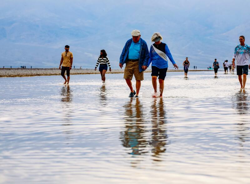 Park visitors kayak, paddle board and wade knee deep in Lake Manly in Badwater Basin.