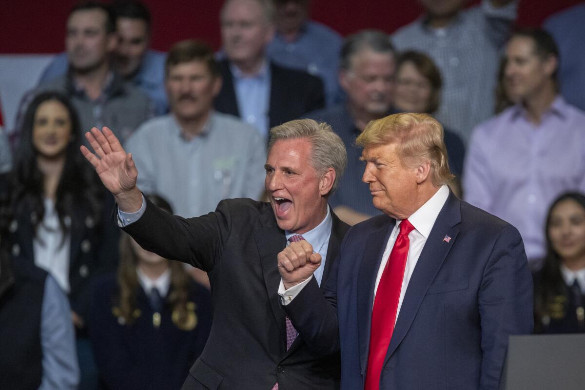 Two white men in suits wave in front of a crowd.