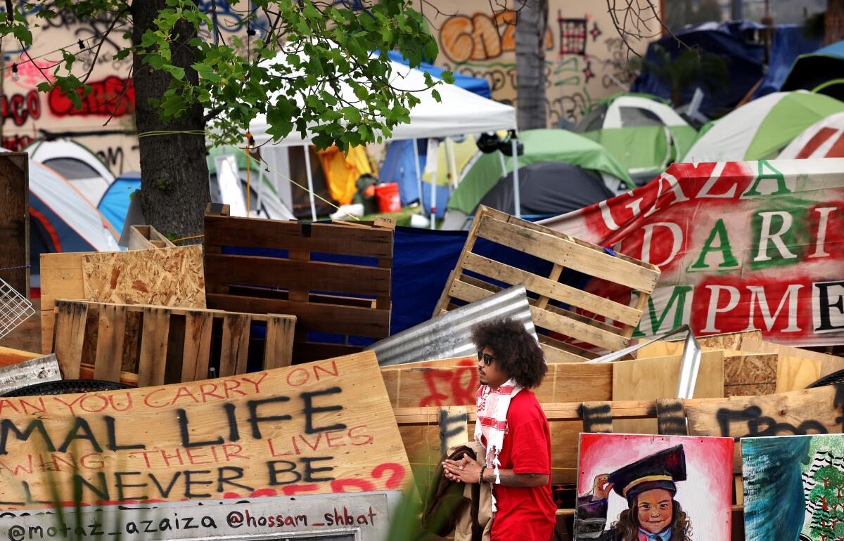 A young man in red walks past an encampment barricaded in plywood. .