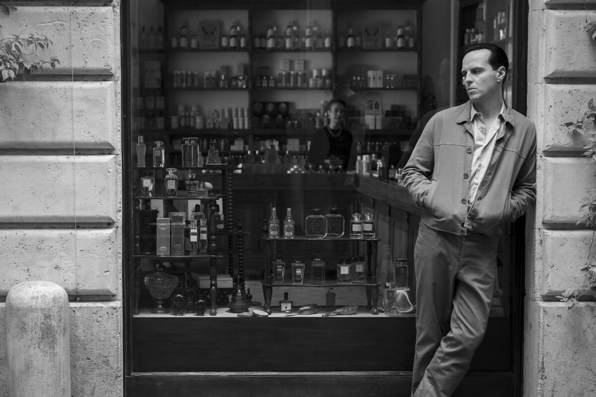 A man leans on the edge of a building in front of a shop window.