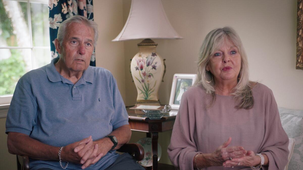 A man in a blue polo shirt sitting next to a woman in a pink top.