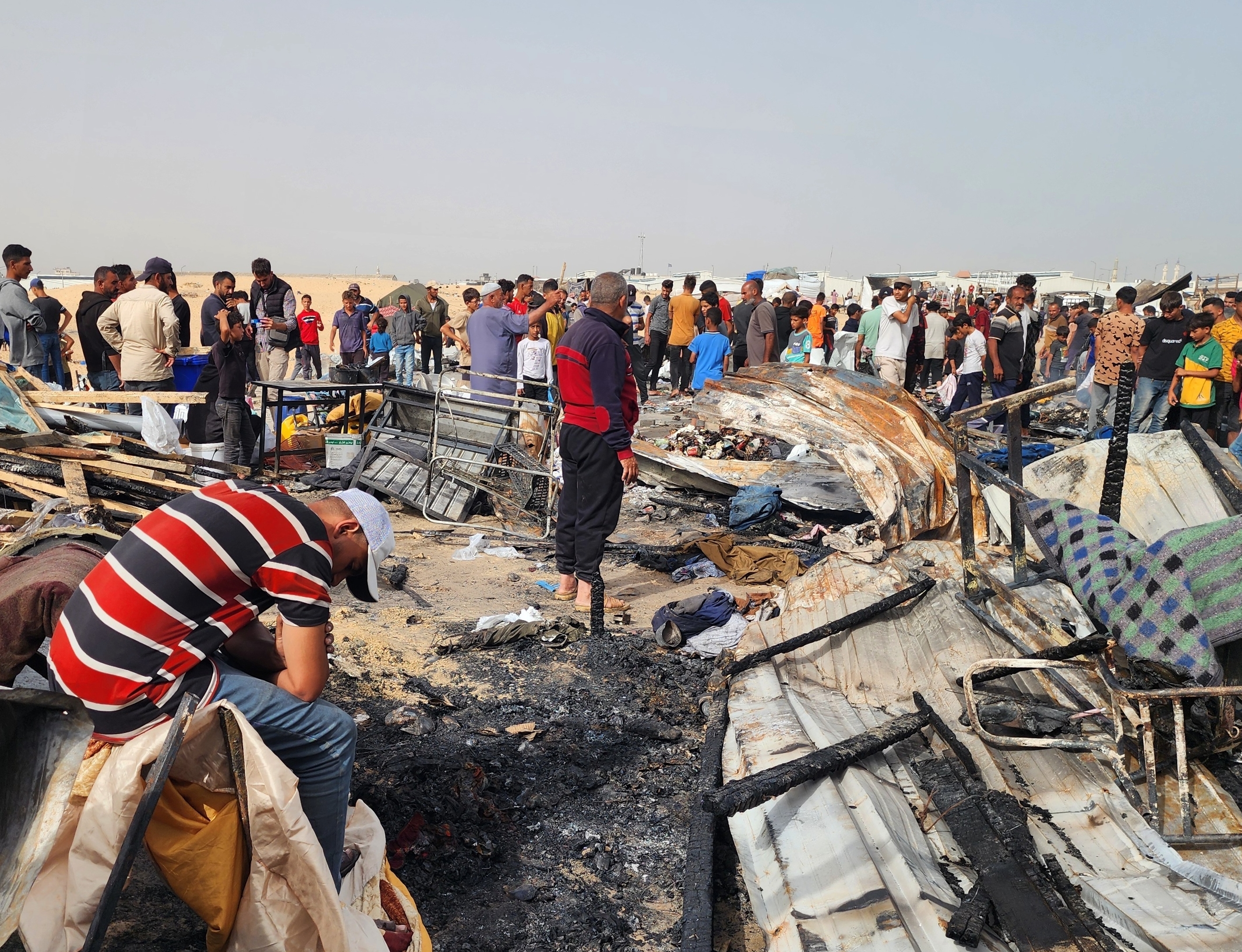 Palestinians stand amongst the burnt wreckage of their tents following the fire