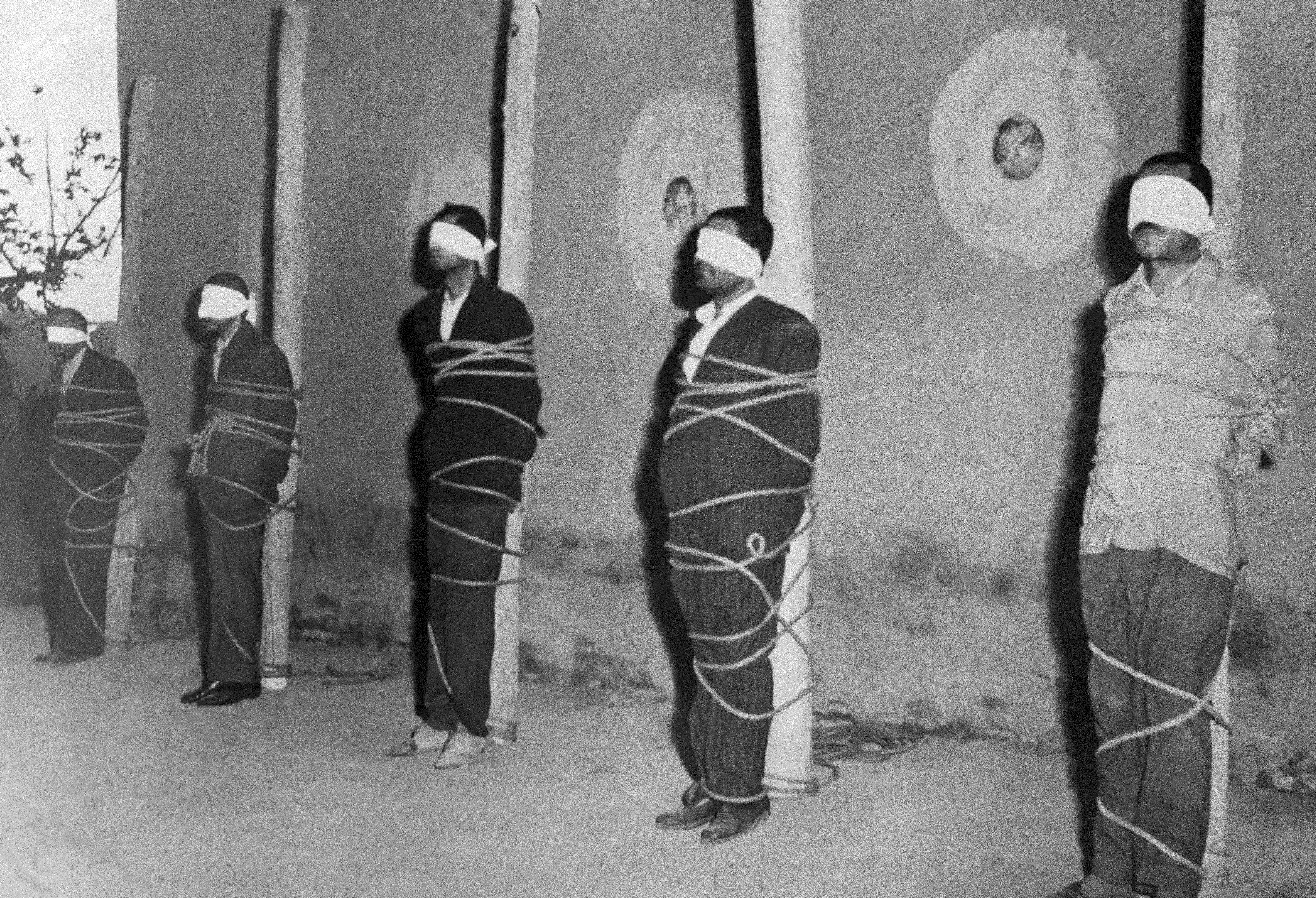 Blindfolded and bound to stakes, five of ten alleged Communist spies await death before a firing squad in the Ghasr Army Barracks in Tehran