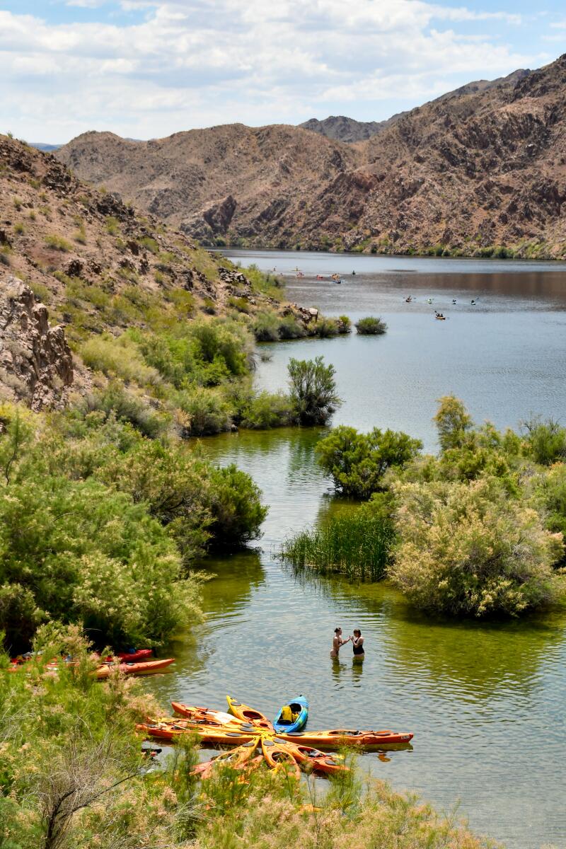 People stand in a river that winds through small islands with trees and tall red-rock hills