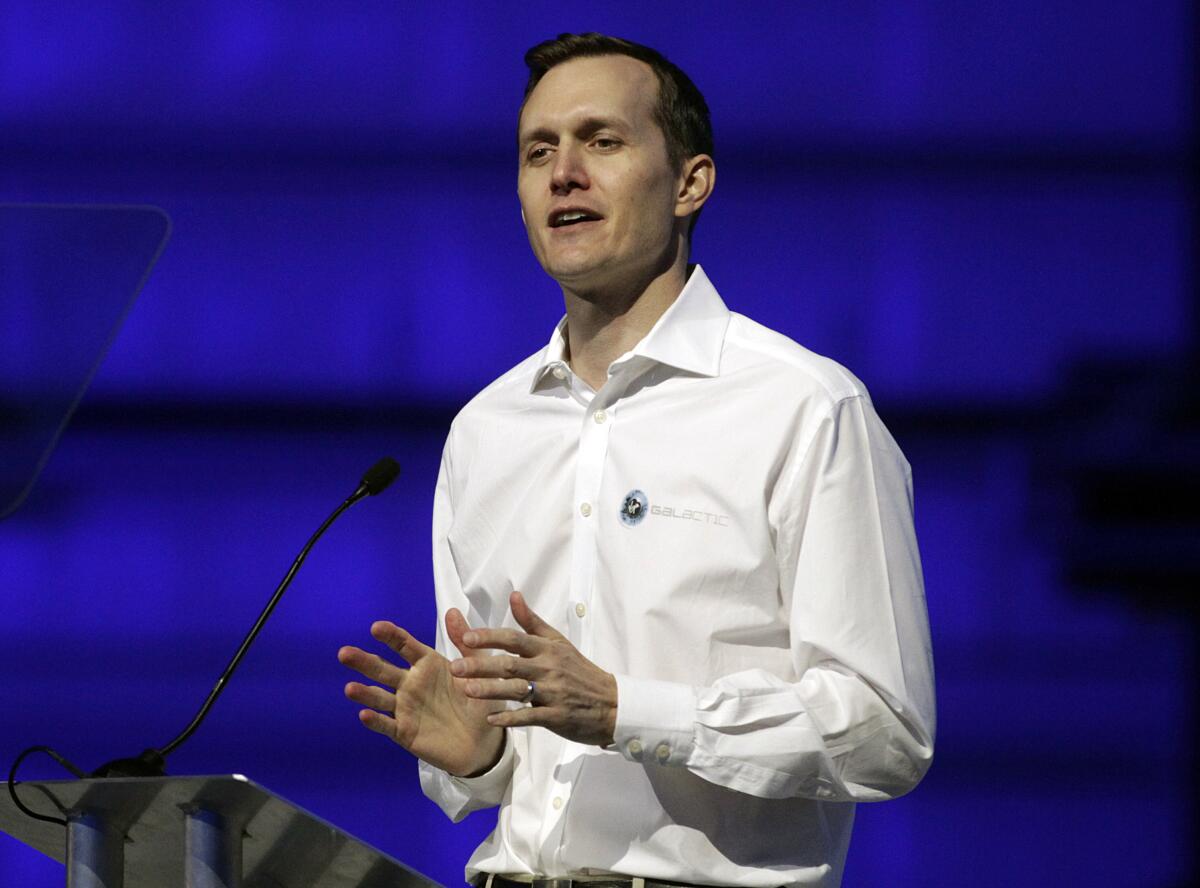 George Whitesides gestures while speaking in a white button-up at a lectern against a cobalt blue background