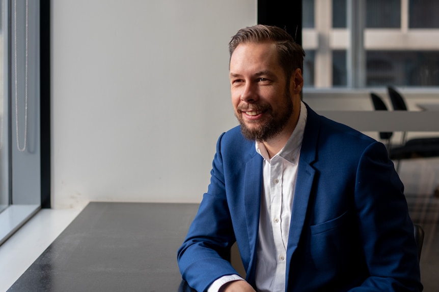 Julian Szafraniec wears a suit and sits at a desk.