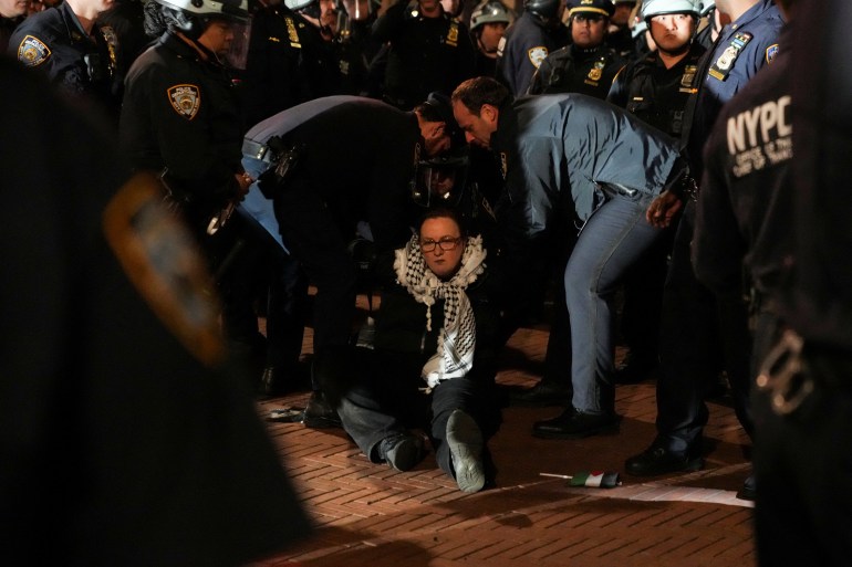 A woman is arrested at Columbia. She is sitting on the floor. Police are around her.