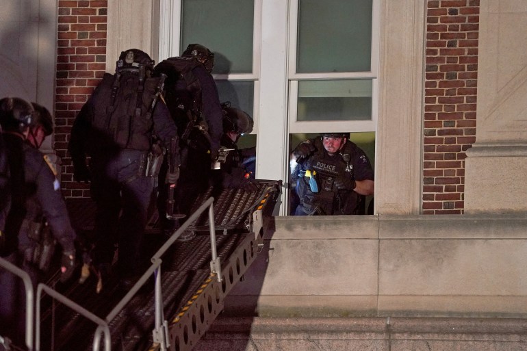 Police officers on a ladder waiting to climb through a window. An officer is already inside.