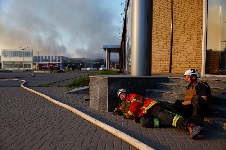 First responders take cover, after the announcement of a Russian missile attack towards Kharkiv, as smoke rises from the site of a household item shopping mall which was hit by a Russian air strike, amid Russia's attack on Ukraine, in Kharkiv, Ukraine, May 25, 2024. REUTERS/Valentyn Ogirenko