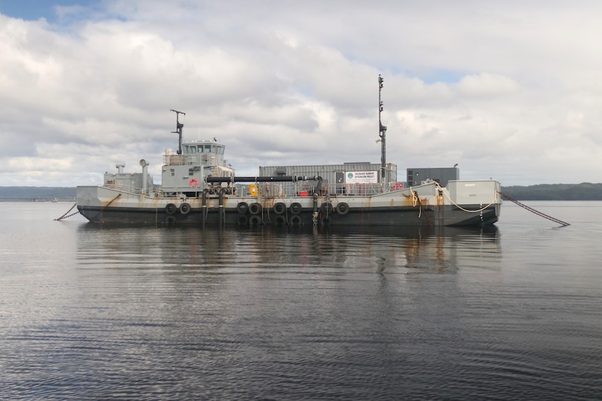 anchored barge with large shipping container sits on grey waters