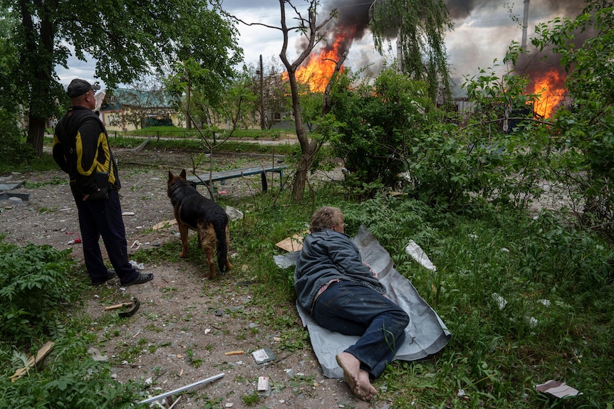 A man lies on the ground as he watches his burning house destroyed by a Russian airstrike in Vovchansk.