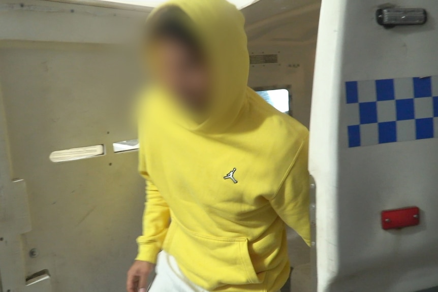 A man in a yellow hoodie in the back of a police car