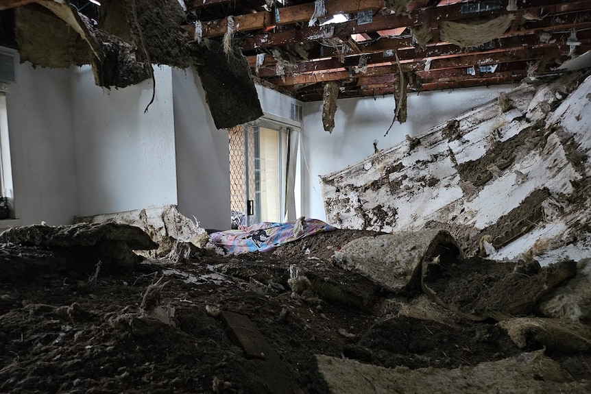 The interior of a house where the the ceiling has fallen through, leaving insulation and drywall piled up.