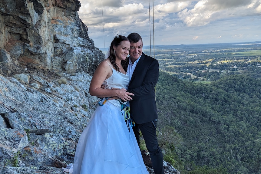 A newlywed couple pose in front of a cave on a mountain.