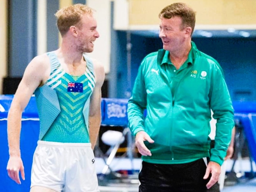 A male gymnast with his coach during a competition.