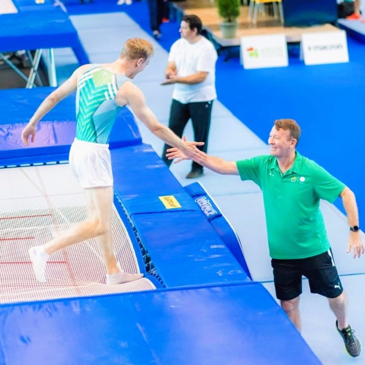 A male trampoline gymnast high fives his coach after a routine.