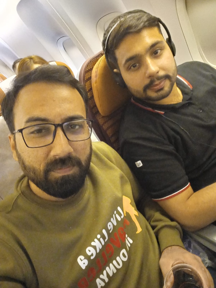 Two men sitting next to each other on a plane, smiling.