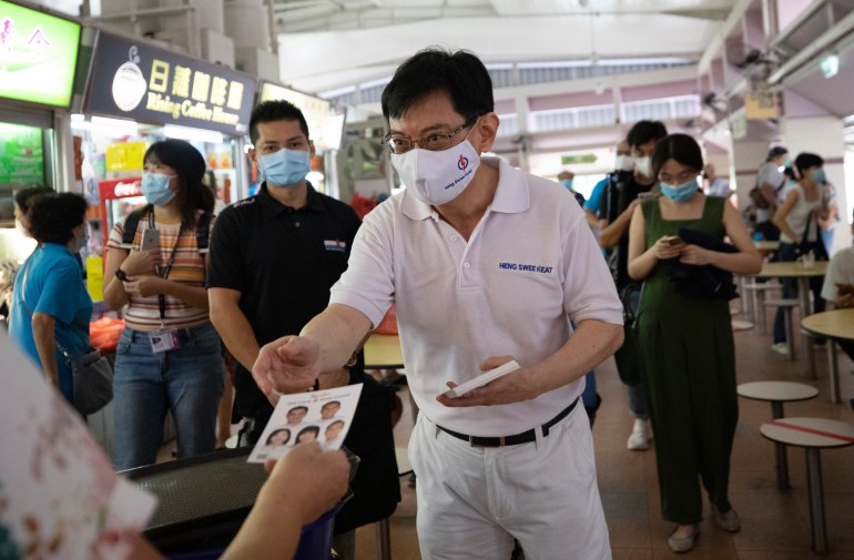 Heng Swee Keat meeting members of the public during the 2020 election campaign. He is wearing white - the colour of the People's Action Party. He is in a hawker centre and there are food stalls nearby. He is handing out leaflets.