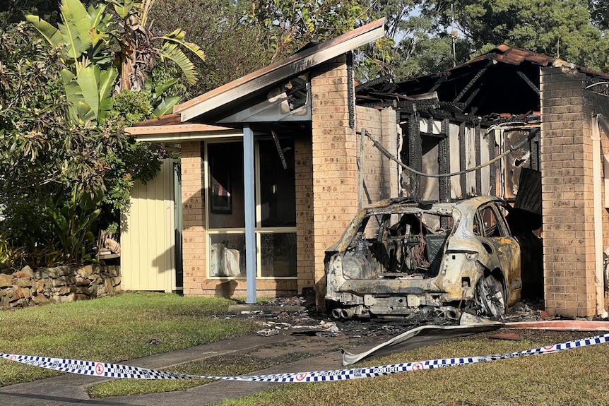 Police tape cuts off a driveway which leads to a burnt out car and home.