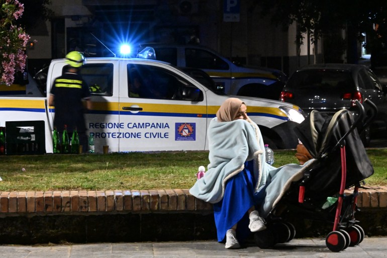 An inhabitant of Pozzuoli sits next to her child's stroller not far from a makeshift camp set up by the civil protection in the port area after a flurry of tremors of a strength not seen in decades was registered in Pozzuoli, on May 21, 2024 - Emergency services in the area reported cracks and pieces falling from buildings, while amateur video from a supermarket in the town of Pozzuoli showed bottles strewn across the floor after being shaken off shelves.