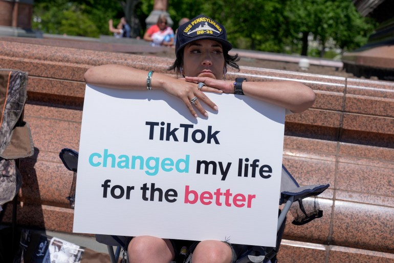 A young person poses with her arms atop a sign that reads, "TikTok changed my life for the better."