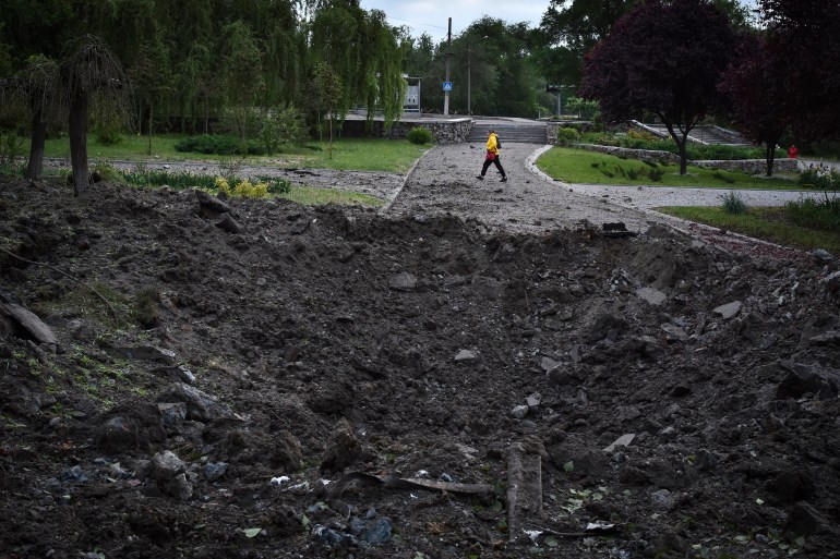 A massive crater left by a Russian missile in an attack on Zaporizhzhia. A woman is walking behind.