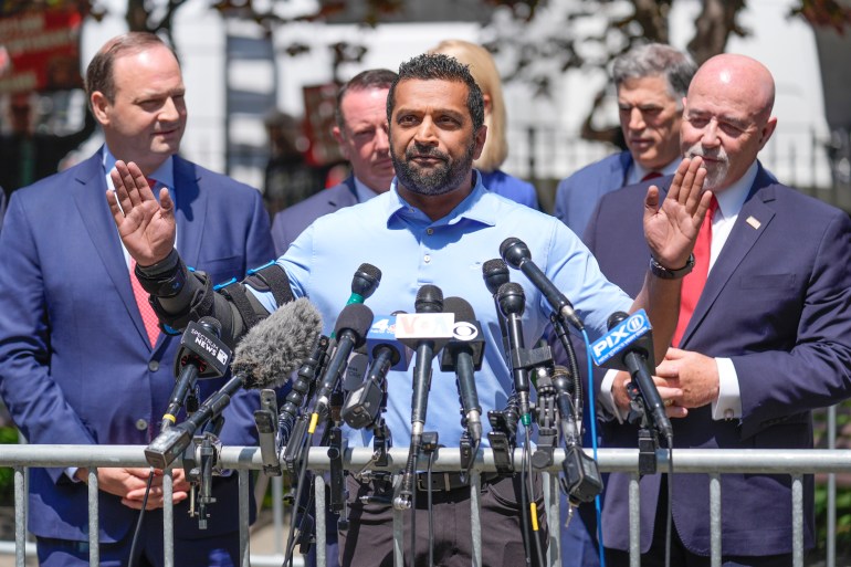 Kash Patel stands behind a row of microphones and a metal barricade as he speaks to the press outside the Manhattan Criminal Court.