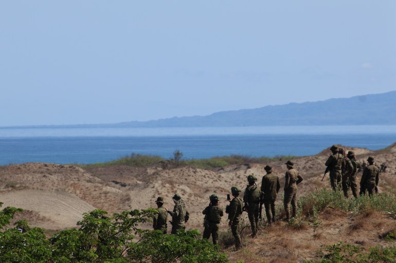 Soldiers lining up on the dunes looking out to sea. Another land mass can be seen in the distance