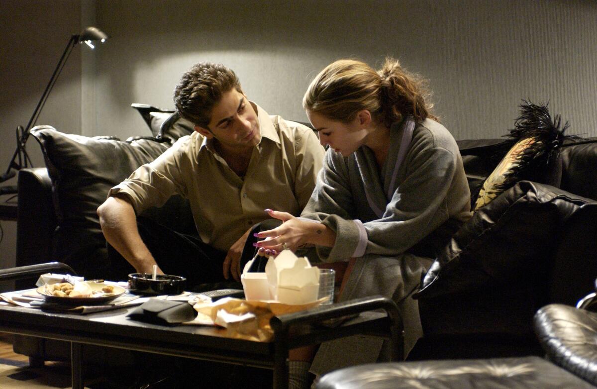 A man and woman sit on a sofa with takeout food in front of them