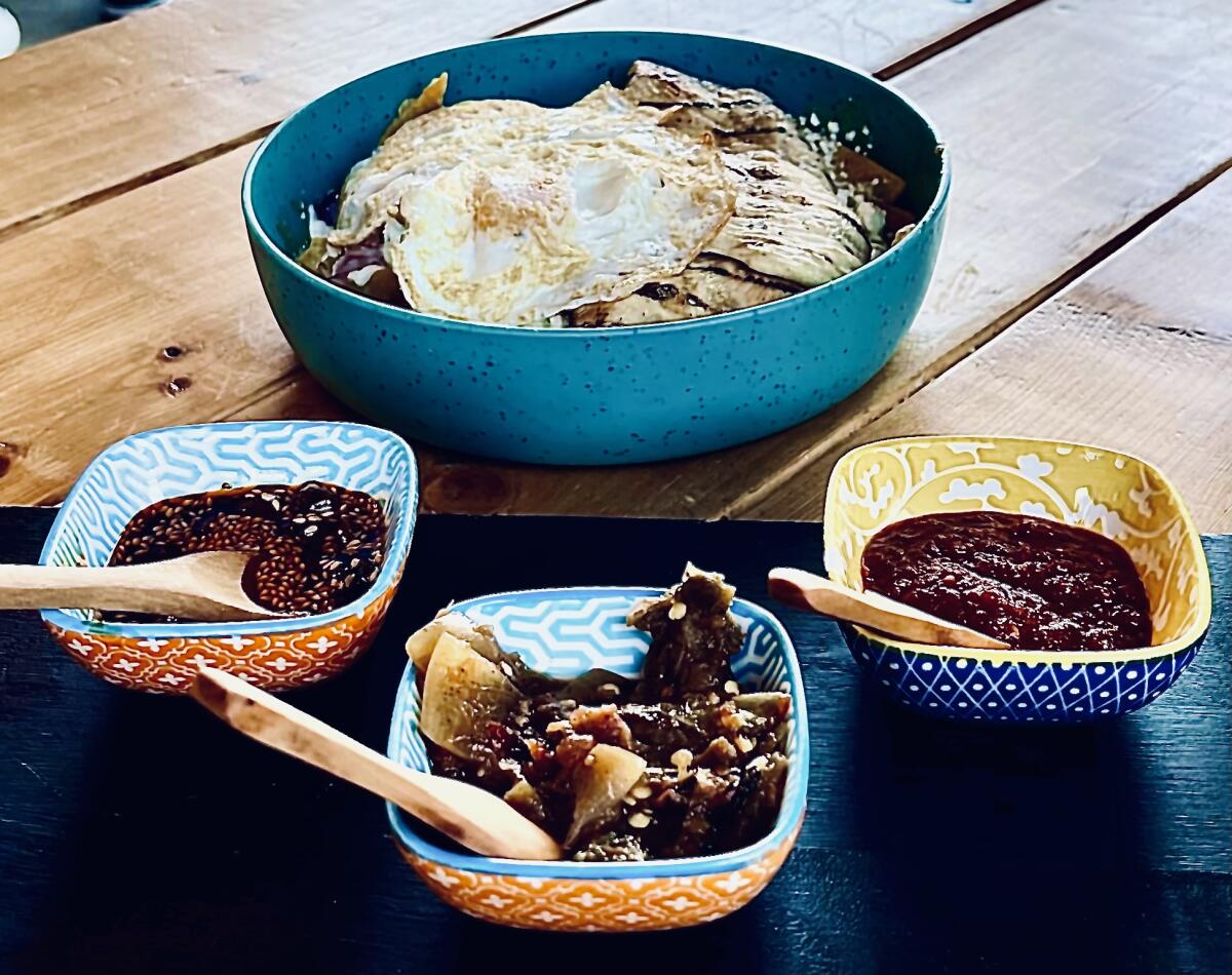 An order of chilaquiles in a large bowl with three smaller bowls of salsas