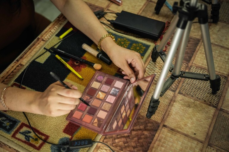 A spread of makeup palettes, brushes, and mascara in front of Sharma which she uses during her recording for makeup. (Md Meharban/Al Jazeera) 