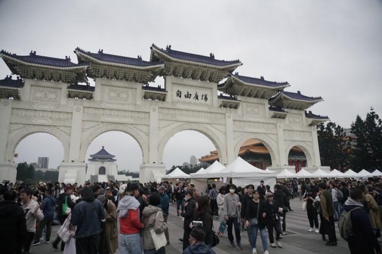 People gathered in Liberty Square to remember the February 28 Incident. They are in front of a ceremonial archway. There are some canopies in front.