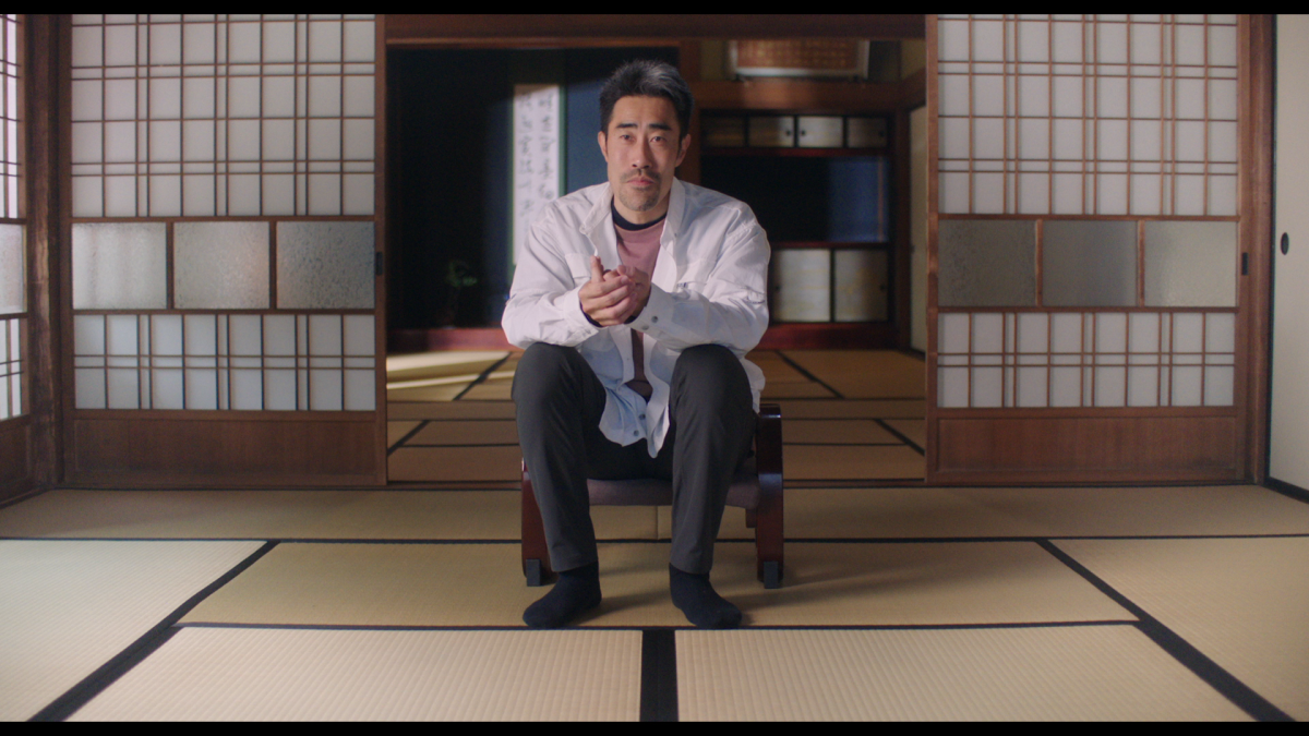 A man in a white shirt and dark pants sits in a room.