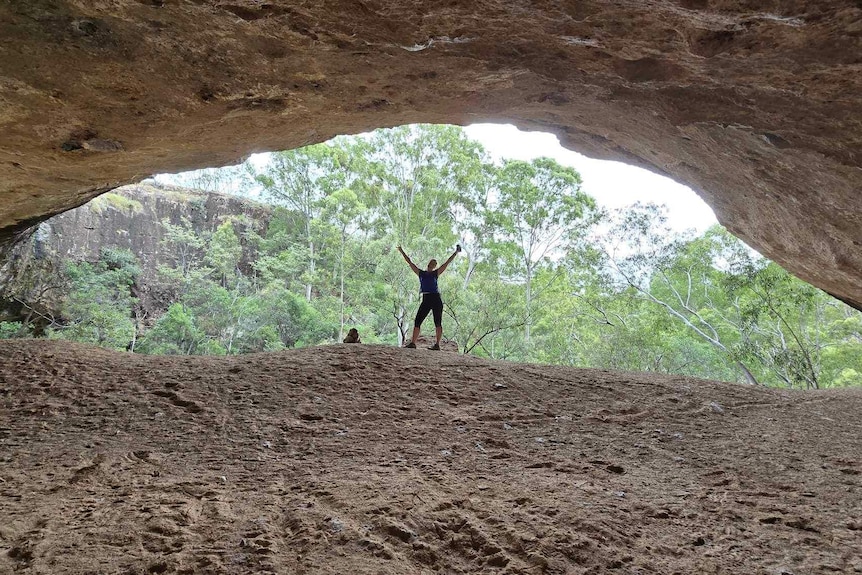 A woman in climbing gear poses triumphantly in a mountain cave.