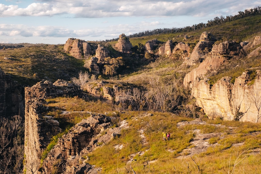 Landscape photo of pagodas and rock formations, with two small hikers on a trail