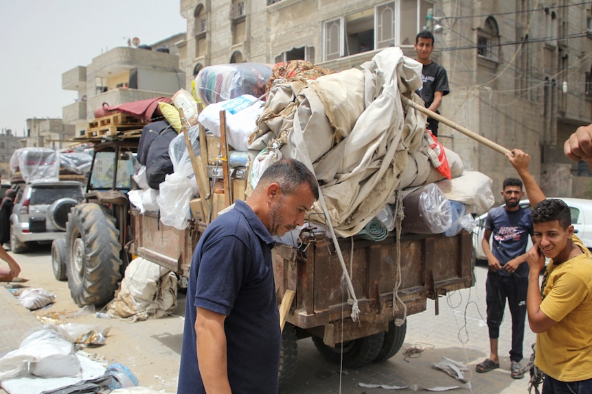 A man and three younger men move a trailer overflowing with goods wrapped in blankets.