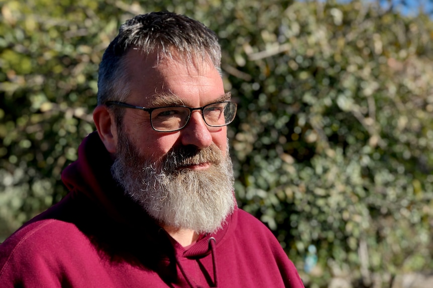 David Caldicott wearing a red hooded jumper and wearing glasses. 