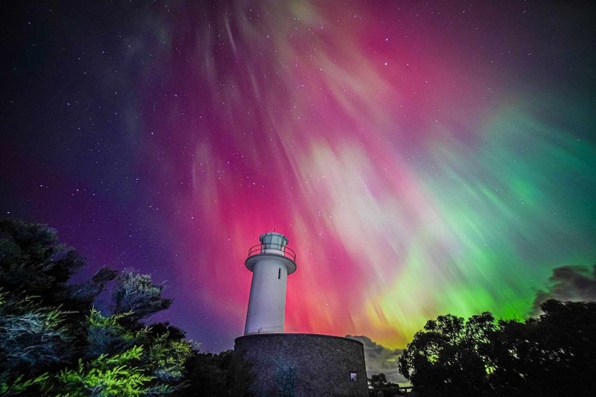 A lighthouse photographed in front of a pink, blue, green and yellow sky