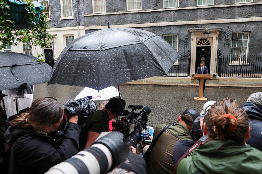 Cameramen and women huddle together in the rain at a press conference